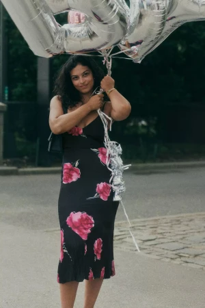 Woman in a black floral dress holding large silver number balloons on an outdoor street