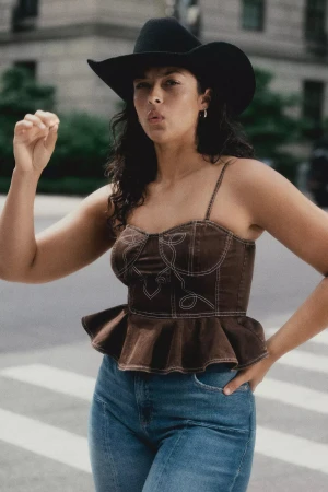 Model wearing a black cowboy hat and brown peplum top with denim jeans outdoors in New York City