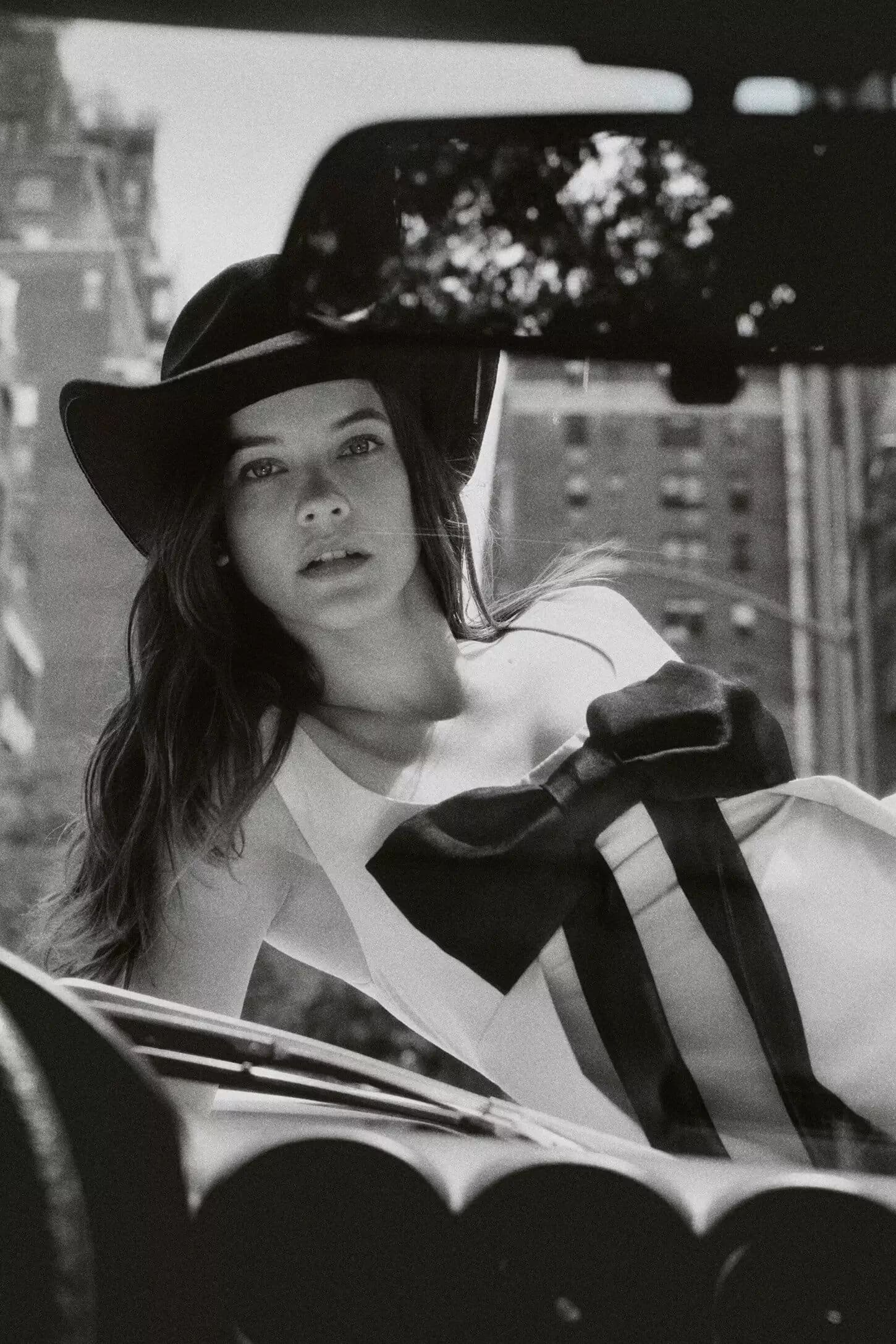 Model wearing a cowboy hat and white dress leaning over a car in New York City for the Anthropologie Fall 2024 campaign.