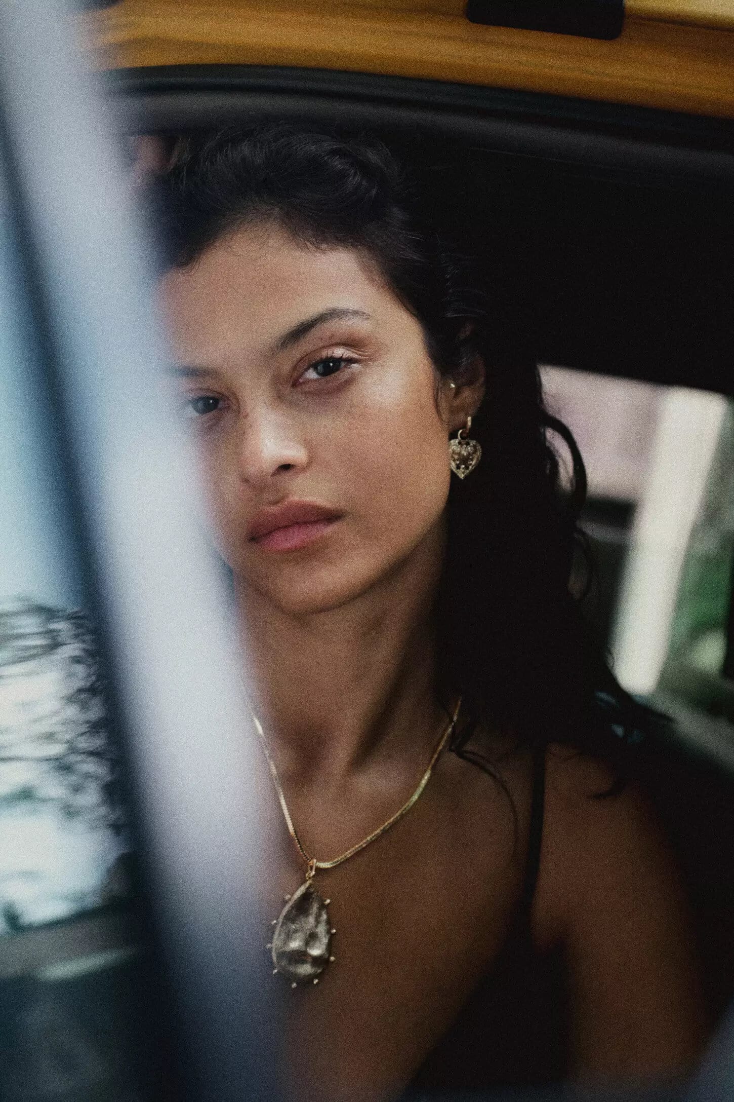 Close-up portrait of a woman wearing gold pendant necklace and earrings looking out from inside a car