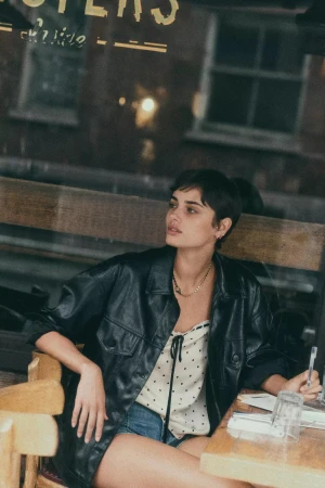 Model Taylor Hill seated at a cafe table wearing a black leather jacket and patterned top