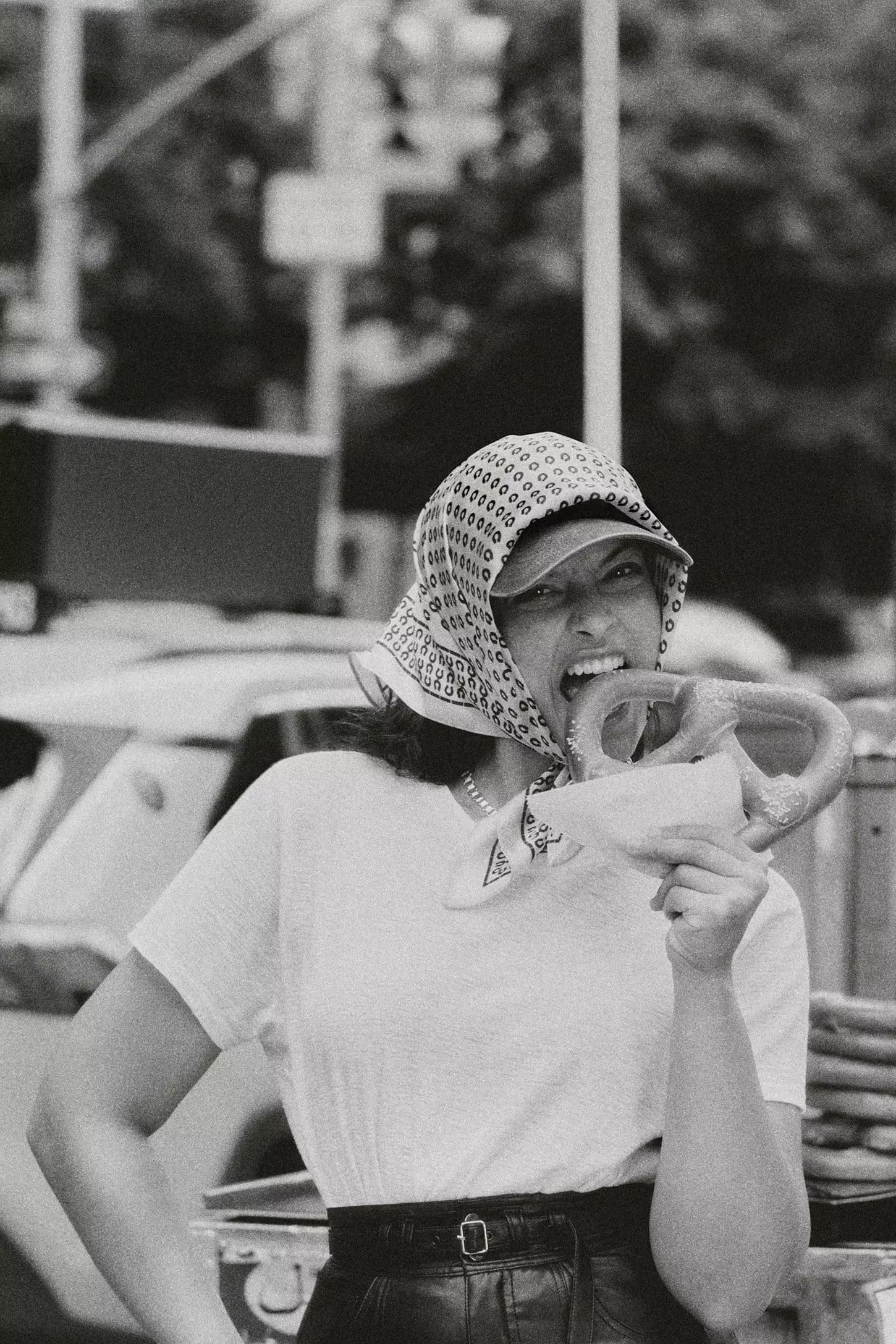 Model wearing a headscarf biting into a pretzel on a city street for Anthropologie Fall 2024 ad campaign