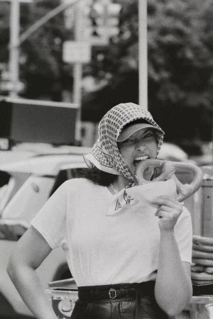 Model wearing a headscarf biting into a pretzel on a city street for Anthropologie Fall 2024 ad campaign