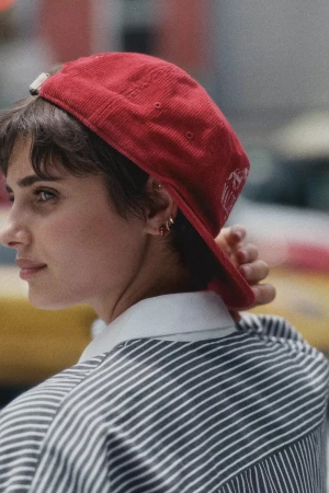 Profile portrait of a woman wearing a red corduroy cap and striped shirt outdoors in New York City.