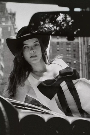 Model wearing a cowboy hat and white dress leaning over a car in New York City for the Anthropologie Fall 2024 campaign.