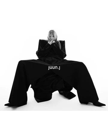 Model wearing structured black coat and trousers against a white seamless background for Juun.J
