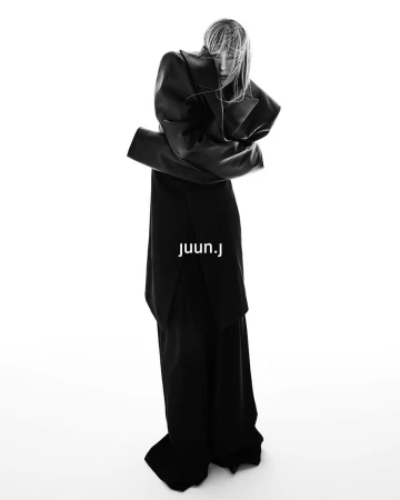 Model wearing an oversized structured black coat and trousers against a white seamless background