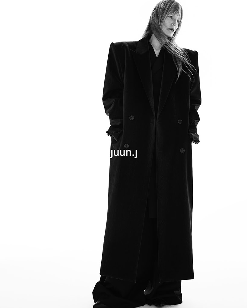 Model Kirsten Owen wearing an oversized black coat with structured shoulders against a seamless white background for Juun.J