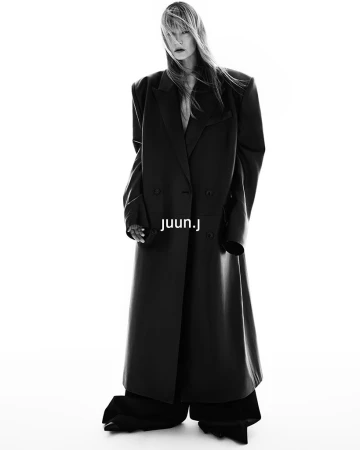 Kirsten Owen in an oversized black coat for the Juun.J Fall 2024 ad campaign, shot in black and white against a plain white background.