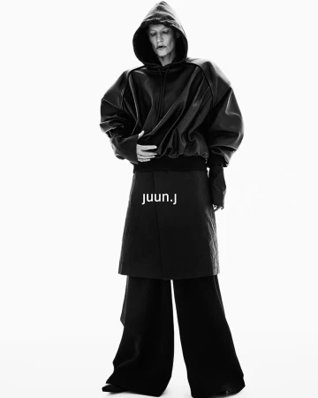 Model wearing a black hooded leather sweatshirt and wide trousers against a solid white background for Juun.J Fall 2024 ad campaign.