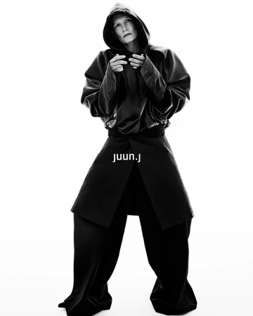 Kirsten Owen in a black hooded sweatshirt and wide trousers against a white seamless background for Juun.J