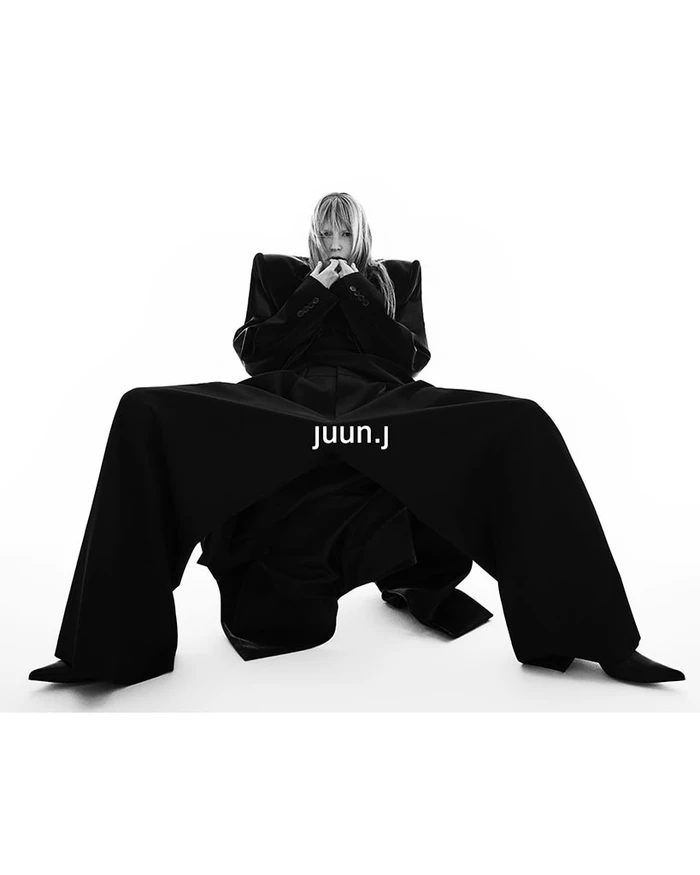 Model wearing structured black coat and trousers against a white seamless background for Juun.J