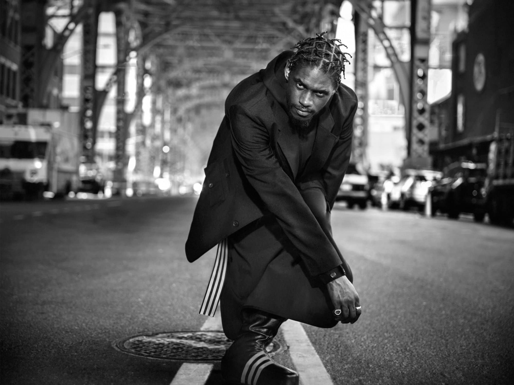 Black and white portrait of A$AP Nast crouching on a city street under an elevated bridge for Y-3 Fall 2024 campaign