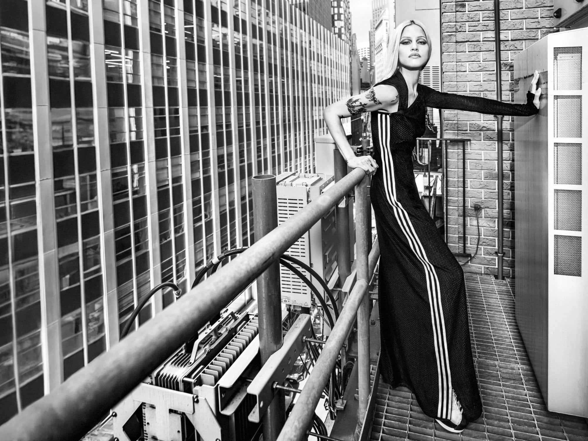 Gabbriette in a black three-stripe dress standing on a rooftop overlooking New York City buildings.