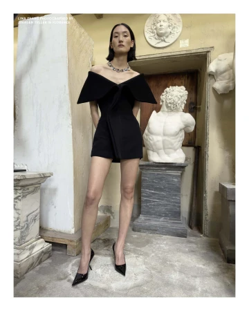 Model Lina Zhang in a black off-the-shoulder dress standing among classical marble sculptures in Florence
