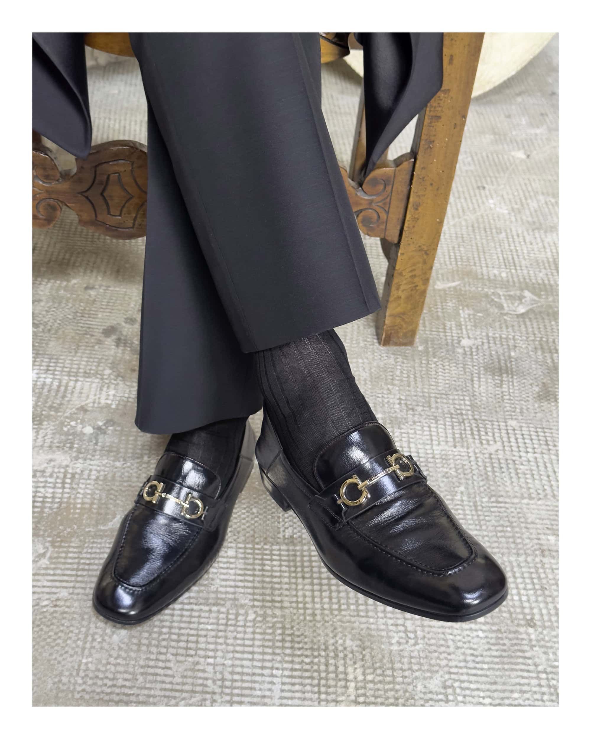 Close-up of black leather loafers with metallic horsebit hardware worn with dark trousers and socks
