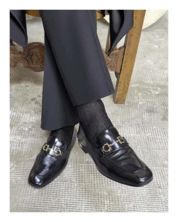 Close-up of black leather loafers with metallic horsebit hardware worn with dark trousers and socks
