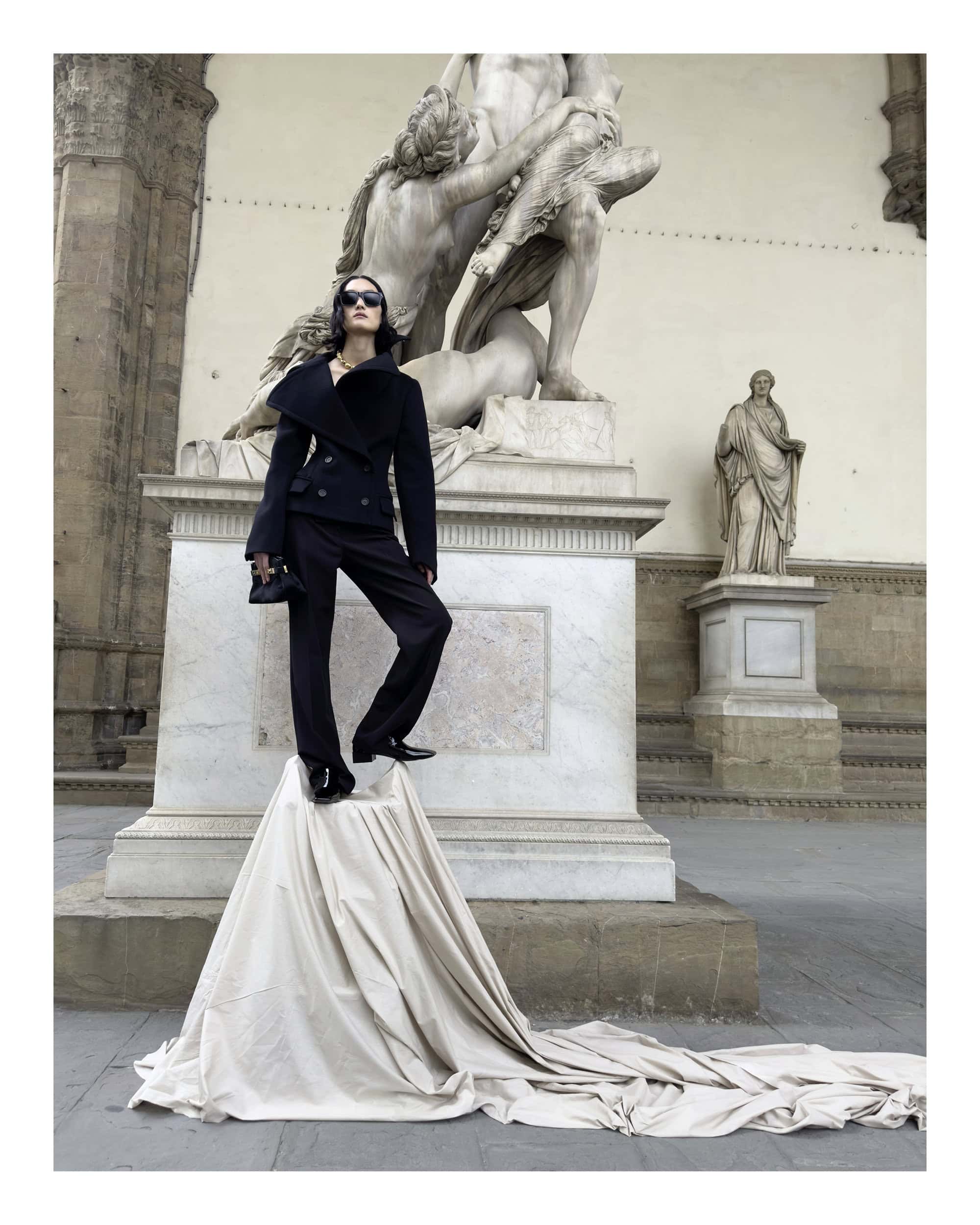 Model standing on a draped pedestal in front of classical sculptures in Florence, Italy for the Ferragamo 2024 ad campaign.