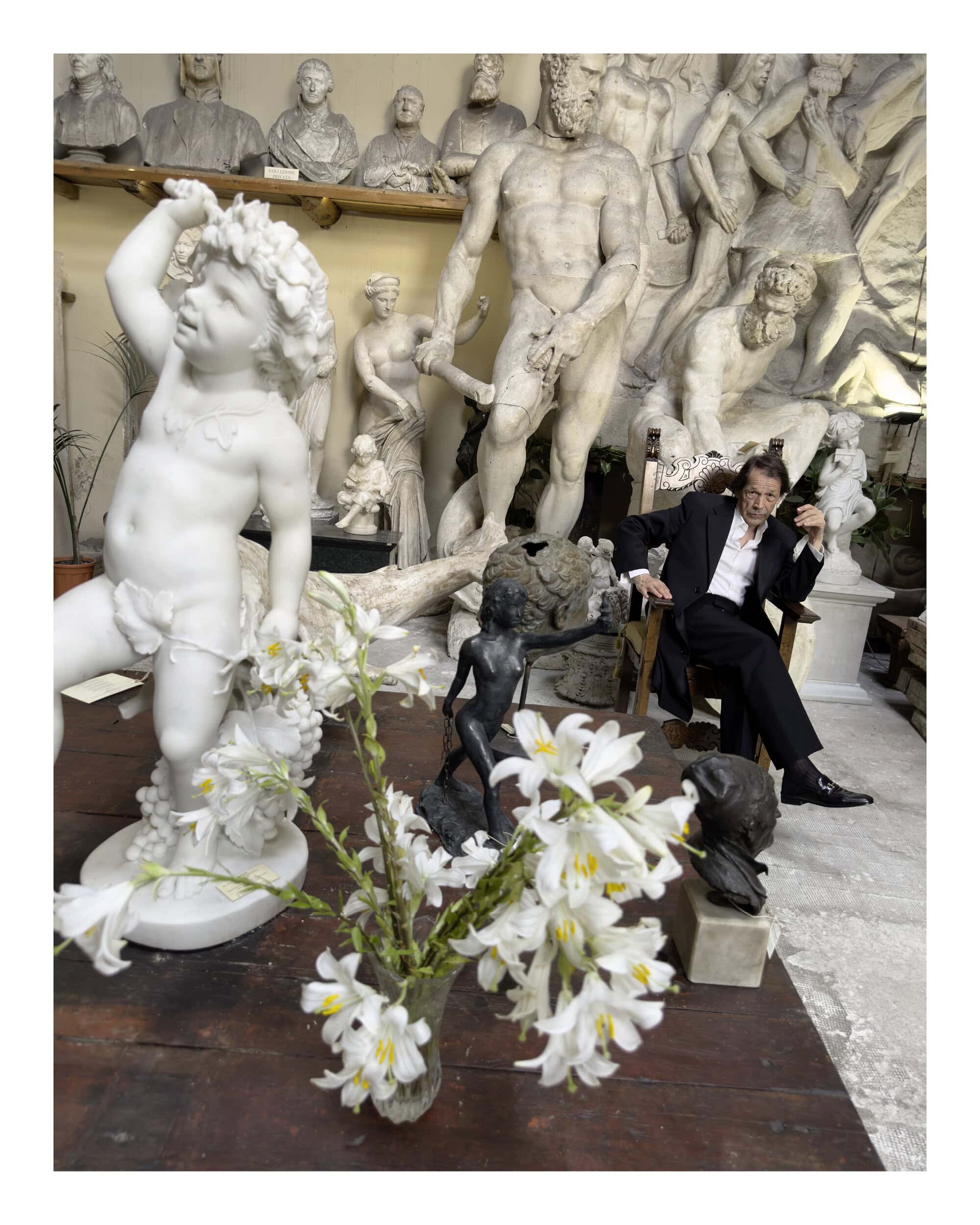 Man seated amongst classical marble statues and white lilies in an Italian studio setting