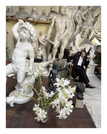 Man seated amongst classical marble statues and white lilies in an Italian studio setting