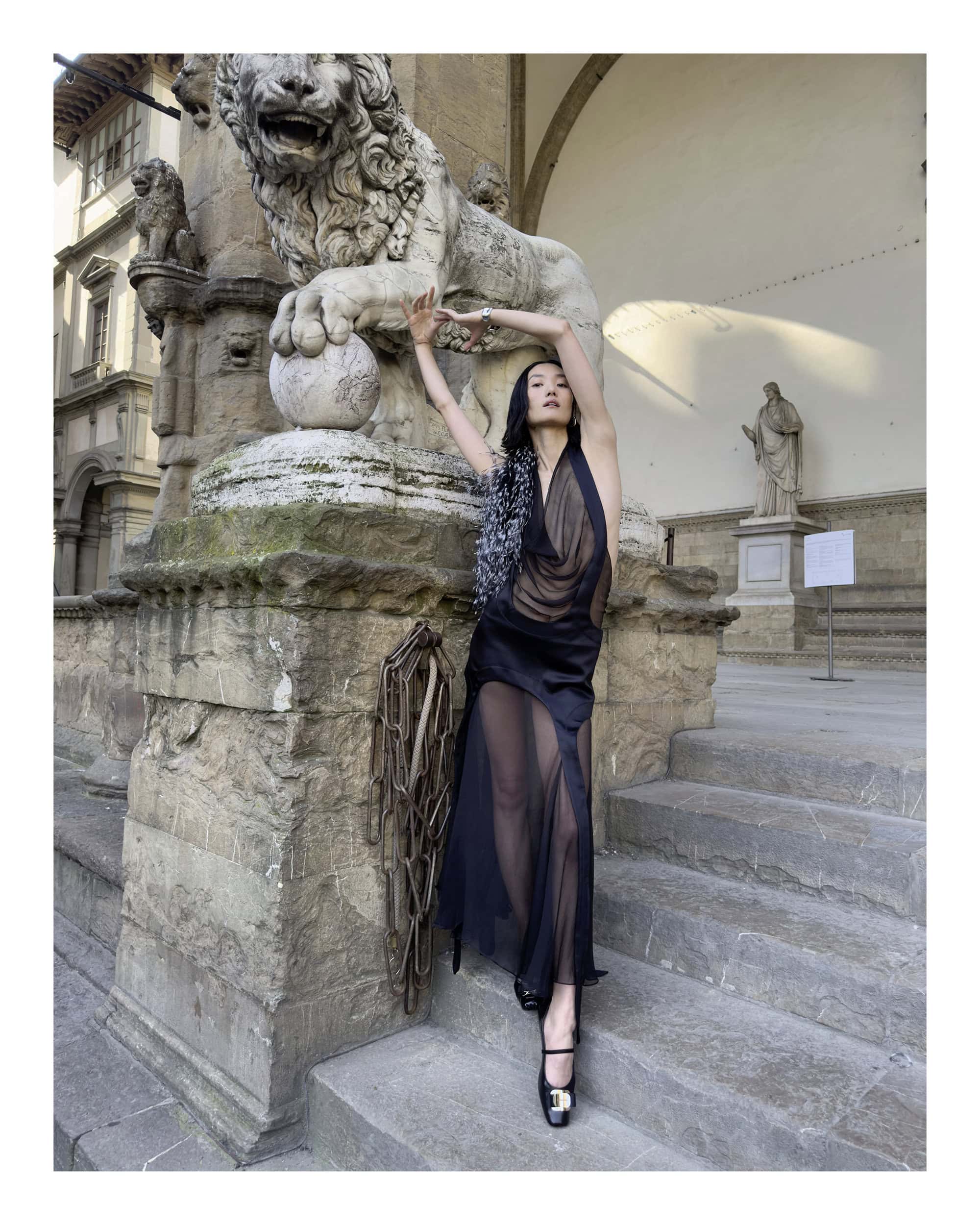 Asian woman in sheer black dress posing next to an ornate stone lion sculpture in Florence for Ferragamo ad campaign.