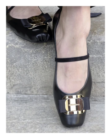 Close-up of black leather Mary Jane flats with gold buckle hardware on stone steps for Ferragamo in Florence campaign.