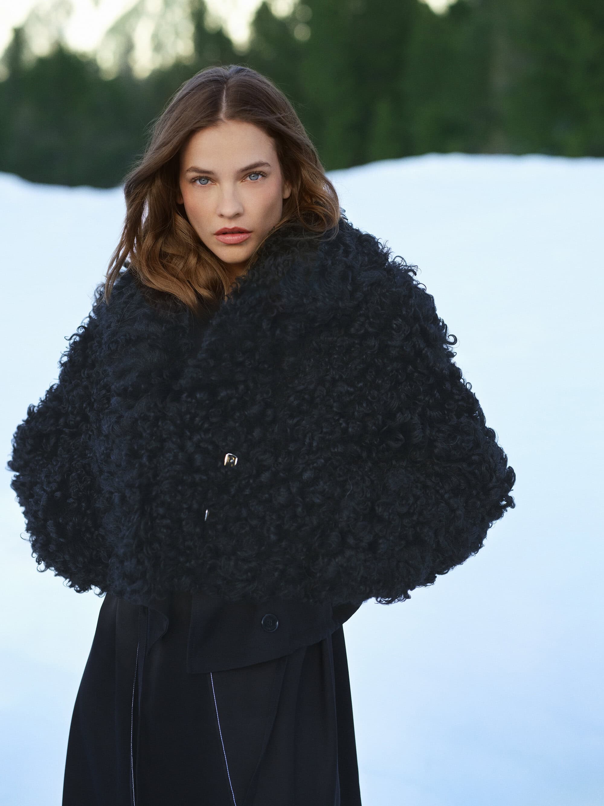 Barbara Palvin wearing a textured black coat against a snowy mountain background for Ports 1961