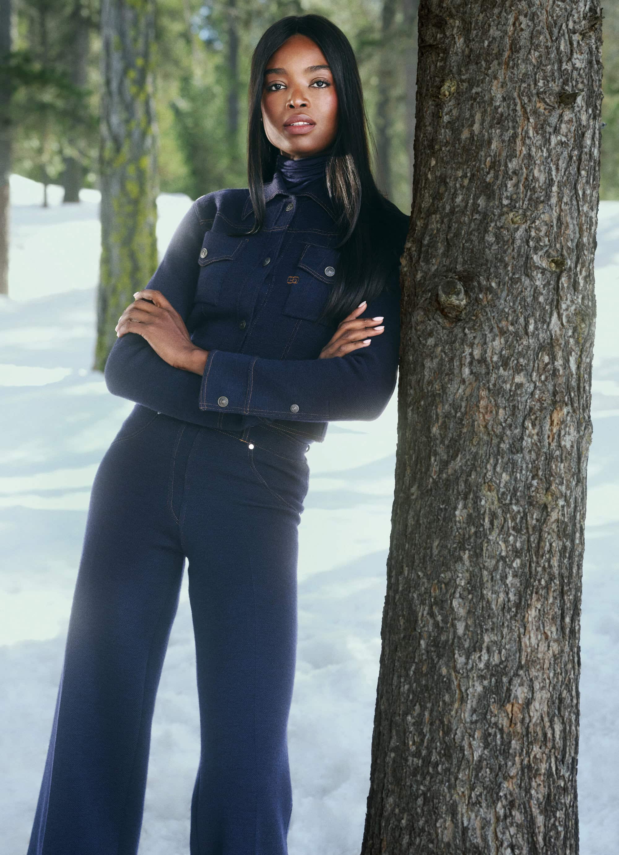 Model Maria Borges in a dark denim jacket leaning against a snow-covered tree in St. Moritz for the Ports 1961 Fall 2024 campaign