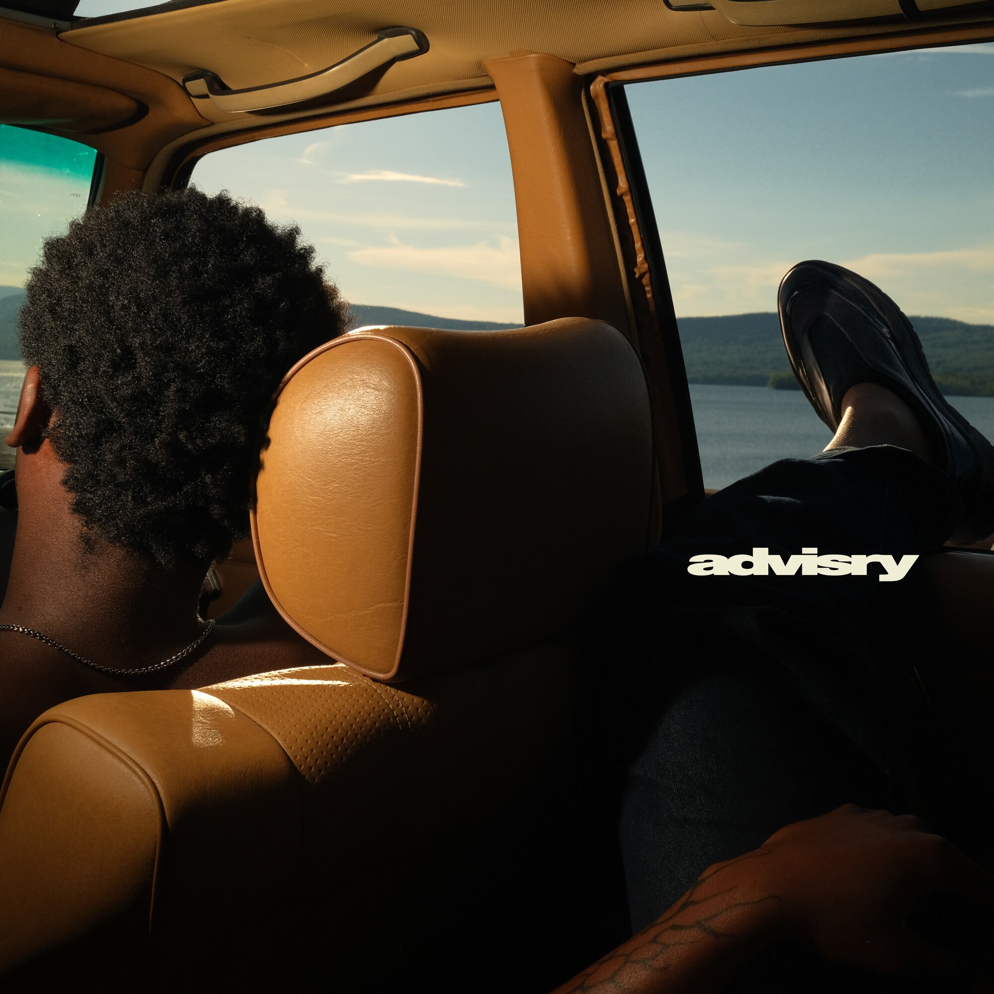 Interior view of a vintage car with tan leather seats and a lake landscape visible through the window.