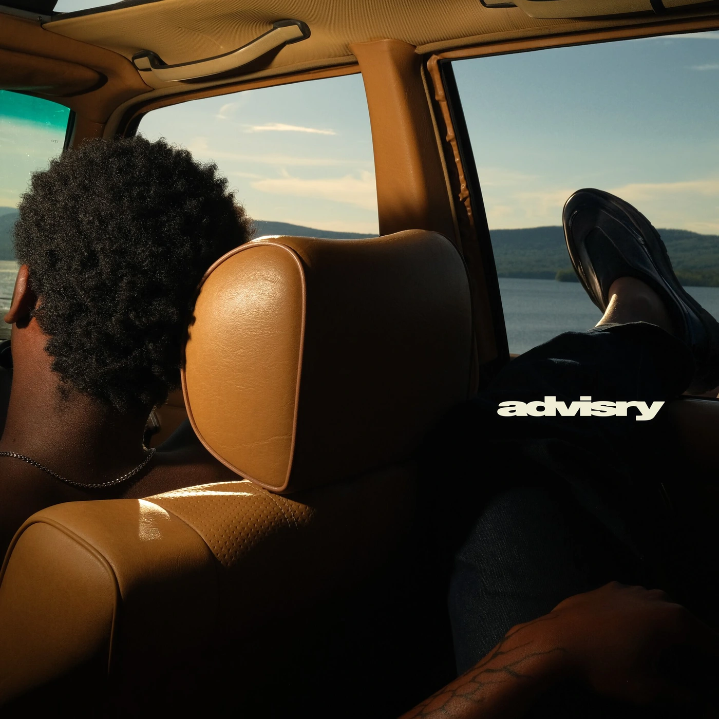 Interior view of a vintage car with tan leather seats and a lake landscape visible through the window.