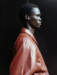 Profile portrait of a Black male model wearing a rust brown leather jacket against a dark background for Sicky Magazine.