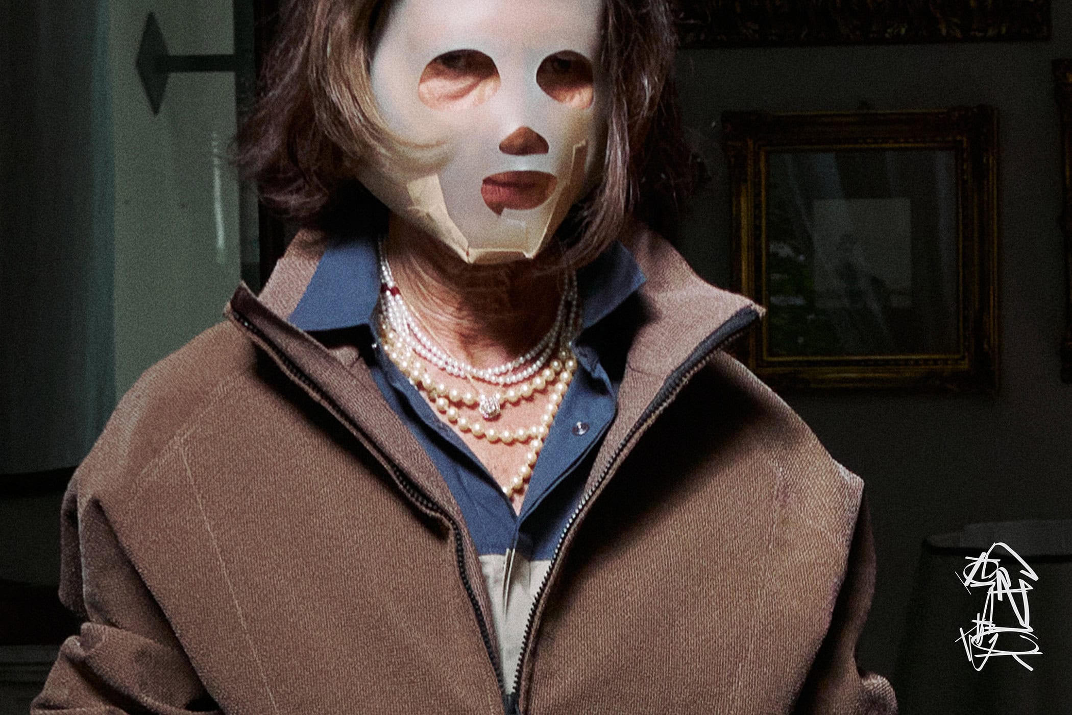Model wearing a white face mask and brown zip-up jacket with layered pearl necklaces, photographed for GR10K.