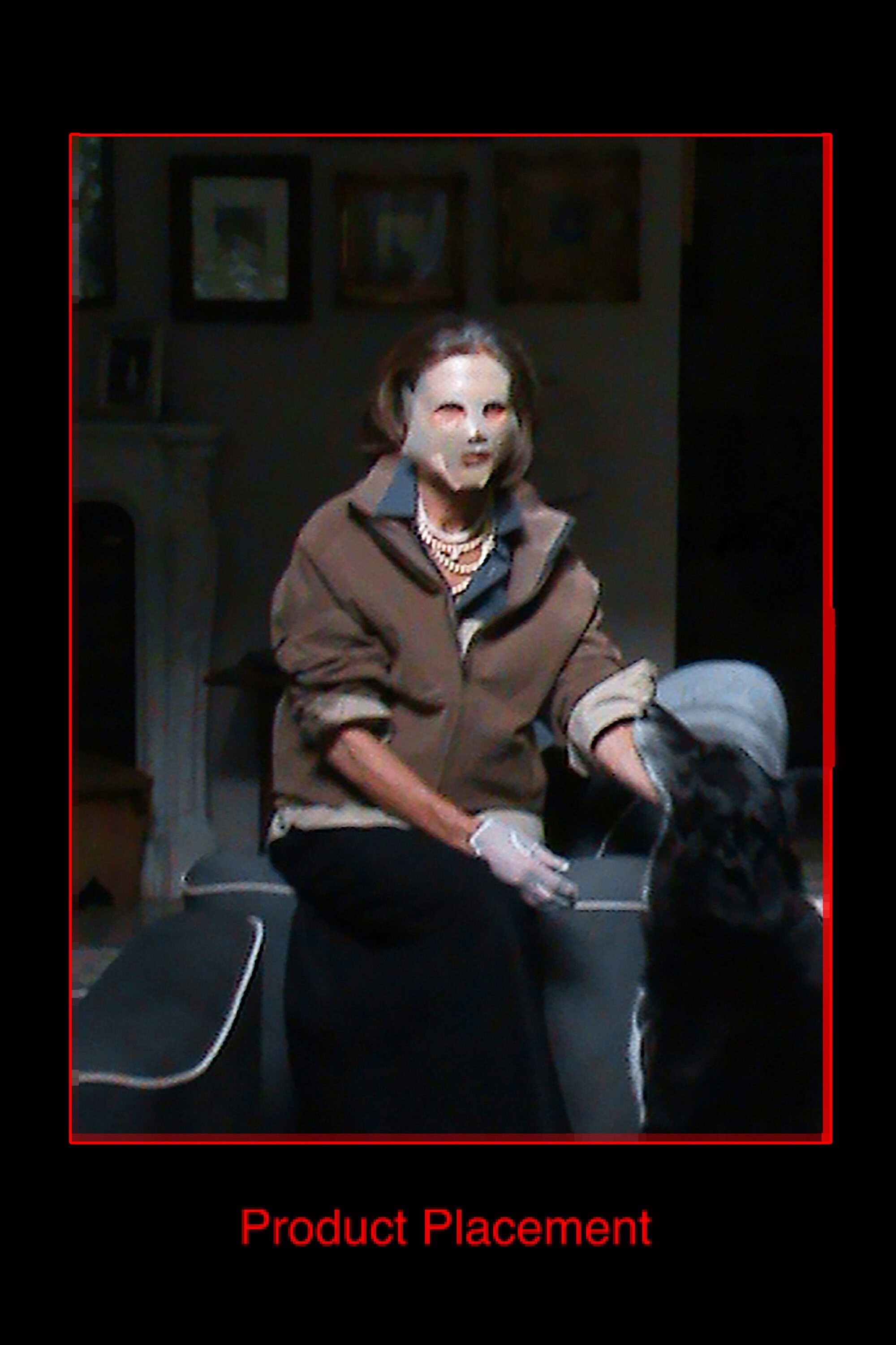 An older woman wearing a face mask and brown jacket sitting indoors with a black dog for the GR10K Incognito campaign.