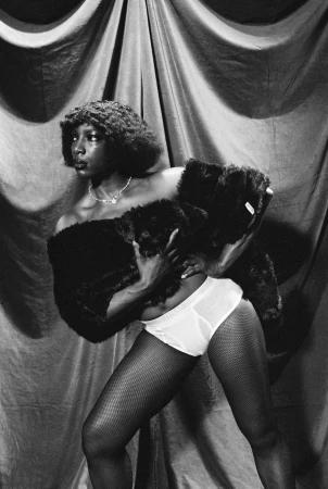 Black woman wearing a dark faux fur stole and white briefs against draped fabric