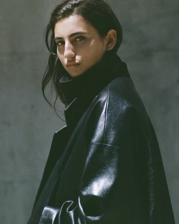 Close-up portrait of a woman wearing a black leather coat against a textured grey background