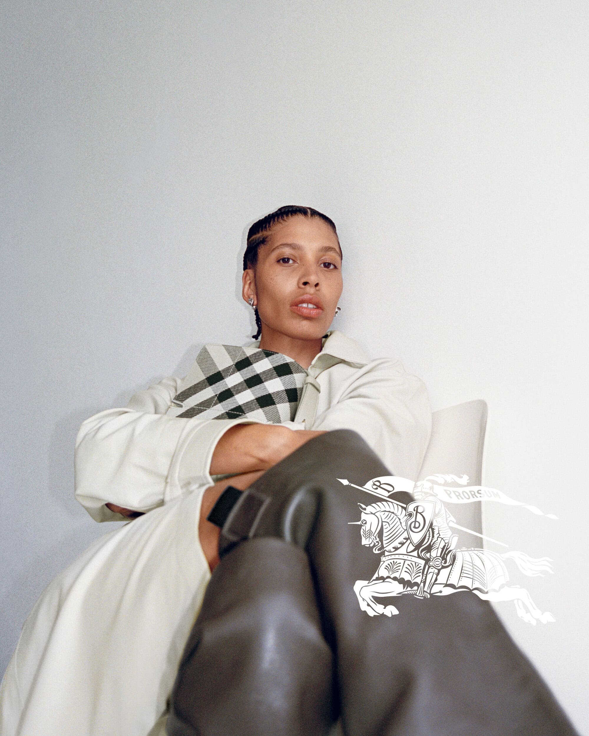 Model wearing a light coat and holding a checked handbag against a white background for Burberry
