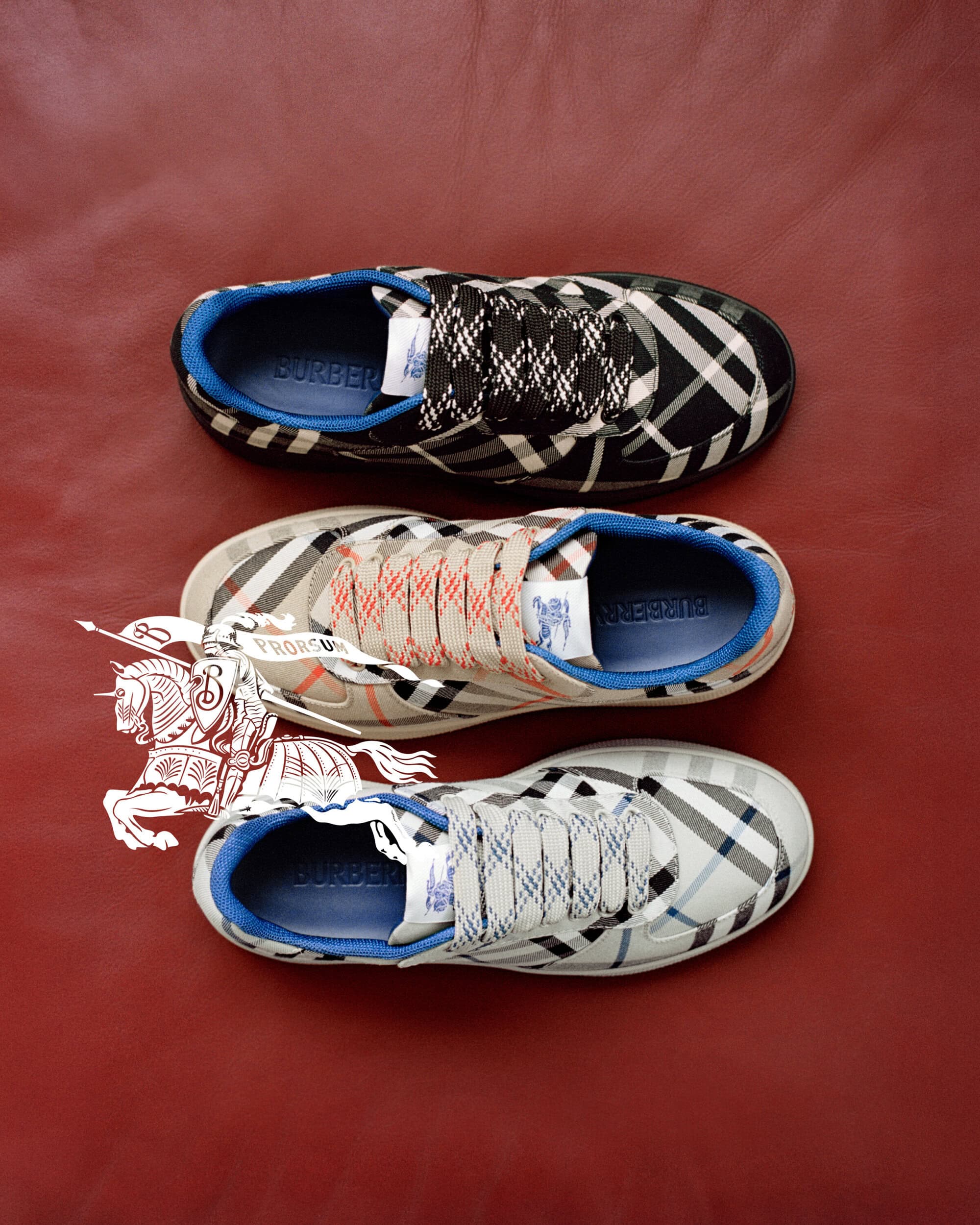 Three pairs of Burberry plaid sneakers arranged vertically on a rich red leather background with a white Equestrian Knight graphic.