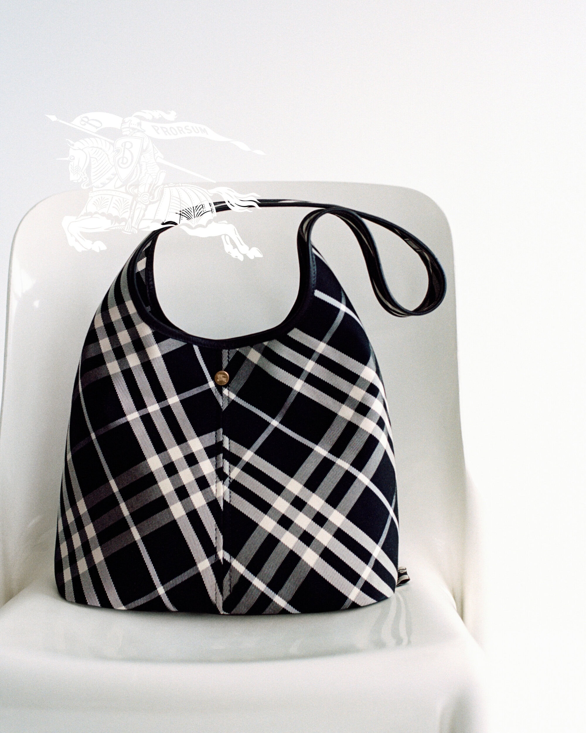 Burberry black and white plaid hobo bag resting on a white chair against a plain white background