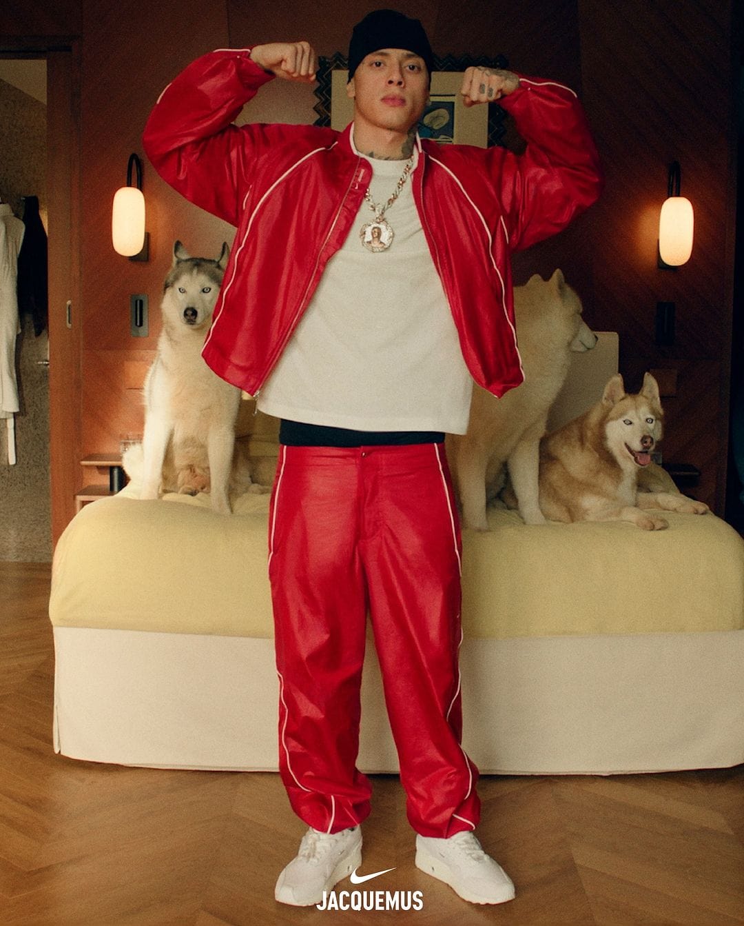 Central Cee in a red jacket and matching pants posing in front of a bed with huskies for Jacquemus x Nike