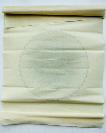 Close-up of rolled parchment paper featuring a faint circular design, creating a textured and artistic background.
