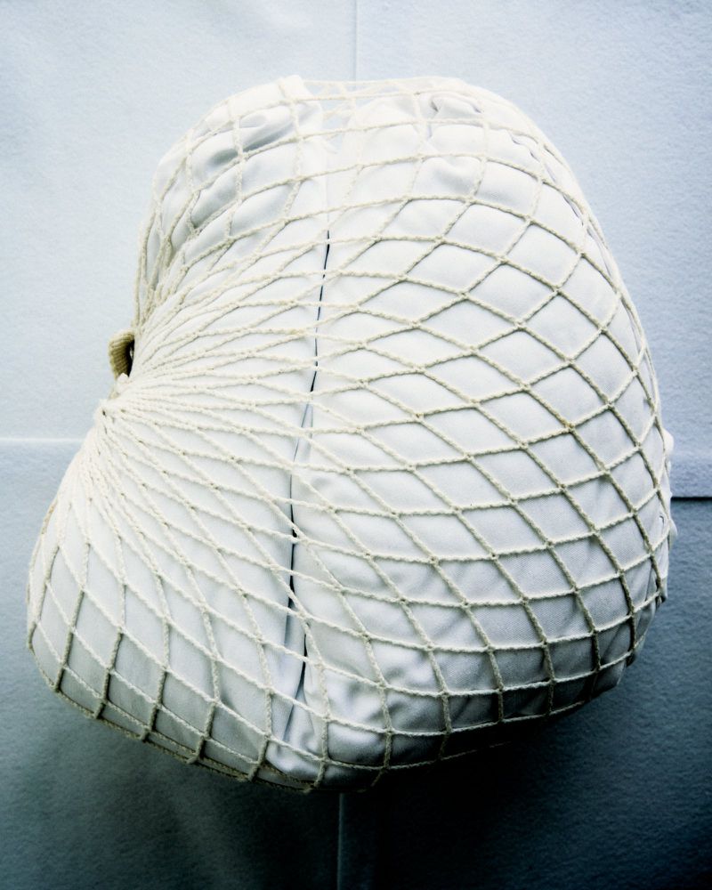 Close-up studio shot of a white cushion covered with a netted, diamond-patterned material, against a clean, light background.