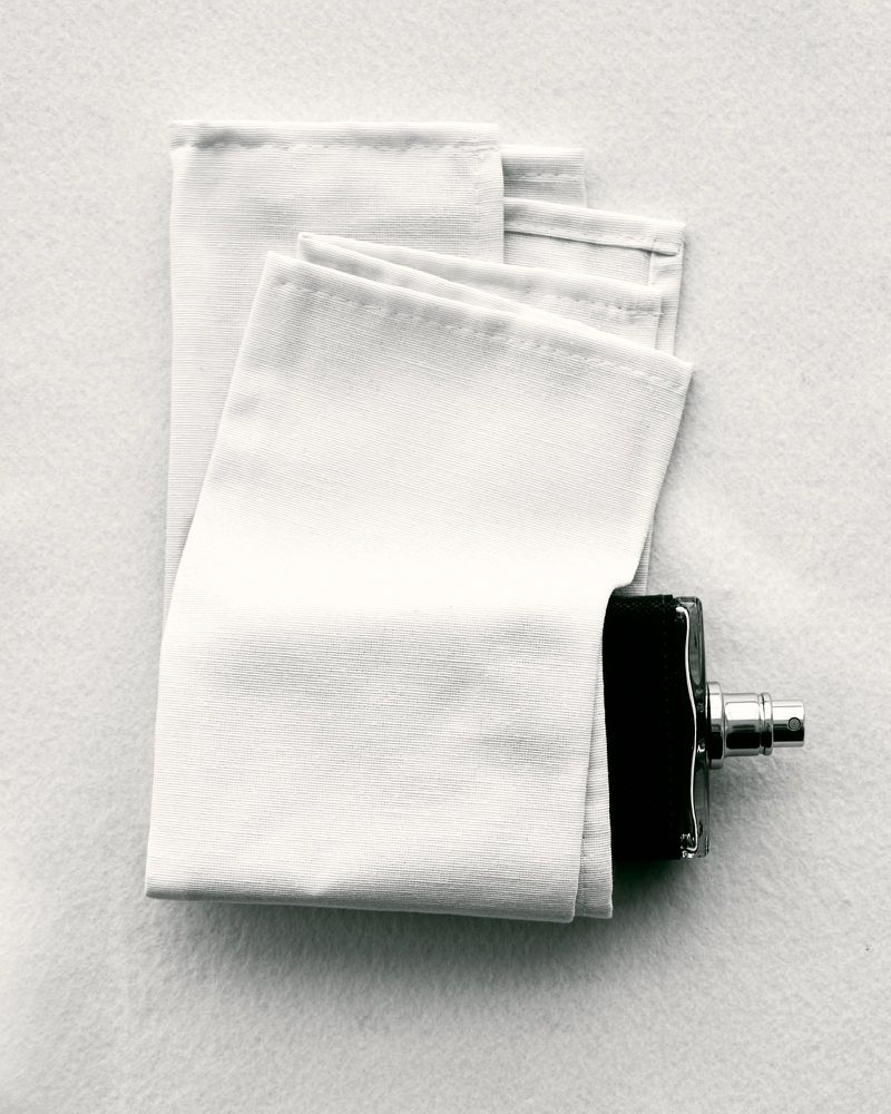 Overhead shot of a bottle of perfume positioned near folded white towels on a textured white background, simple and clean aesthetic.