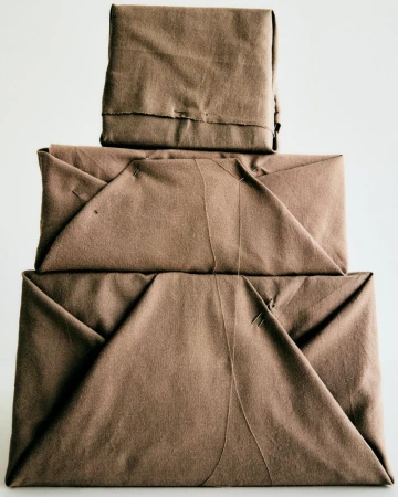 Three neatly wrapped, brown, rectangular packages are stacked on top of each other against a stark white background in a studio shot.