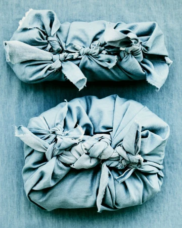 Two gifts wrapped in light blue fabric, tied with matching material, displayed on a coordinating blue fabric background.