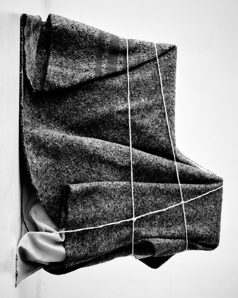 Monochromatic photograph of textured, folded cloth with string tied around it, creating an abstract and dimensional art piece.