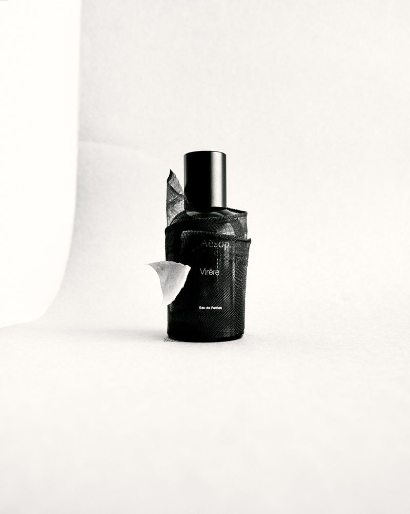 Black Aesop Virere perfume bottle with a black cap and white paper against a solid white background in a studio setting.