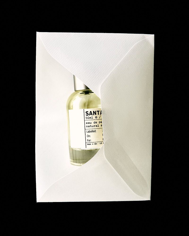 Perfume bottle in a white envelope. The bottle has a white label with black text, and the liquid inside appears light green.