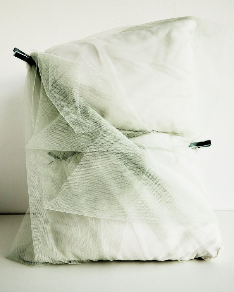 Artful arrangement of pillows and sheer fabric, secured with clothespins, creating an abstract, minimalist composition on a white backdrop.