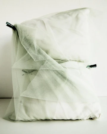 Artful arrangement of pillows and sheer fabric, secured with clothespins, creating an abstract, minimalist composition on a white backdrop.