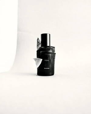 Dark perfume bottle wrapped in dark fabric with a white leaf on a white seamless background